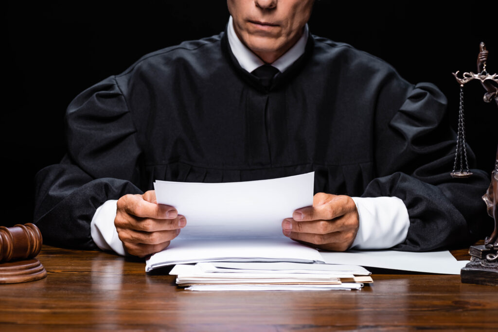 cropped view of judge in judicial robe sitting at table and reading paper isolated on black